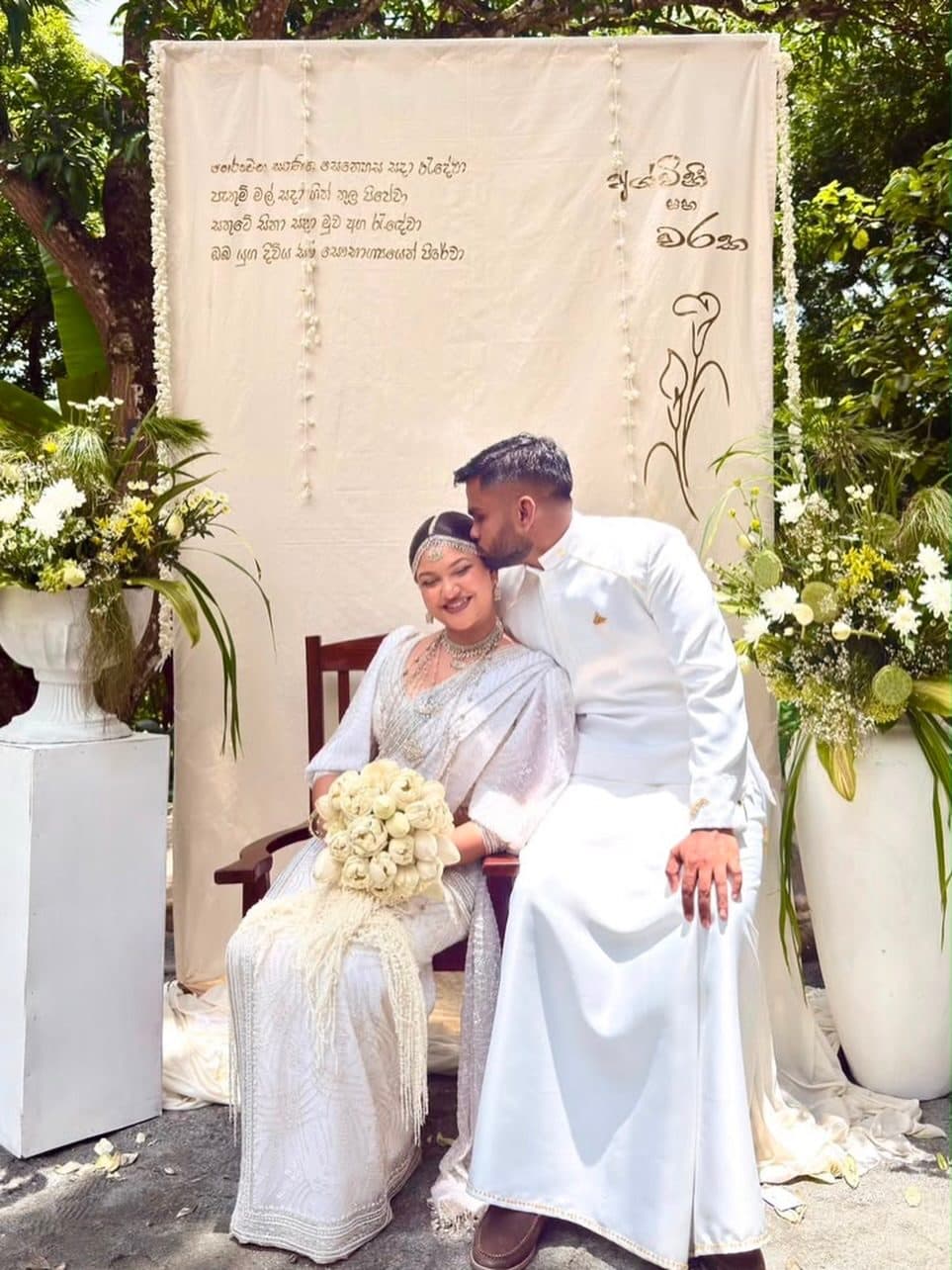 A bride and groom seated before a floral backdrop at the walawwa