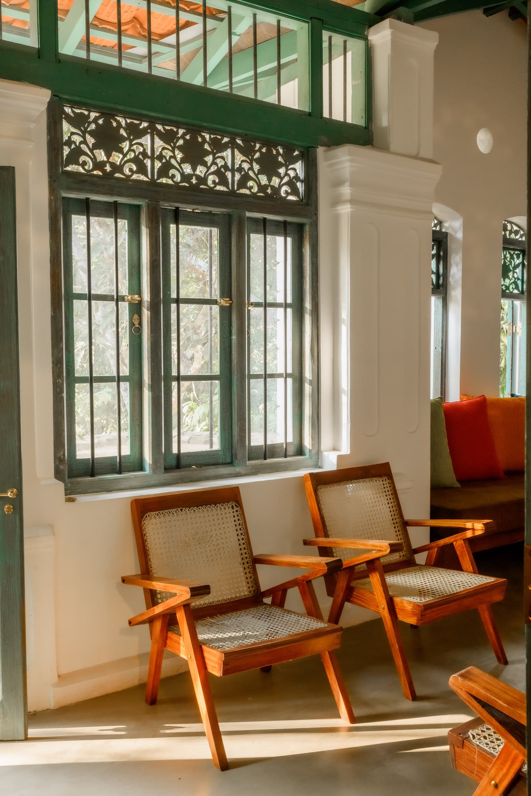 Two cane chairs beside tall green windows in warm light