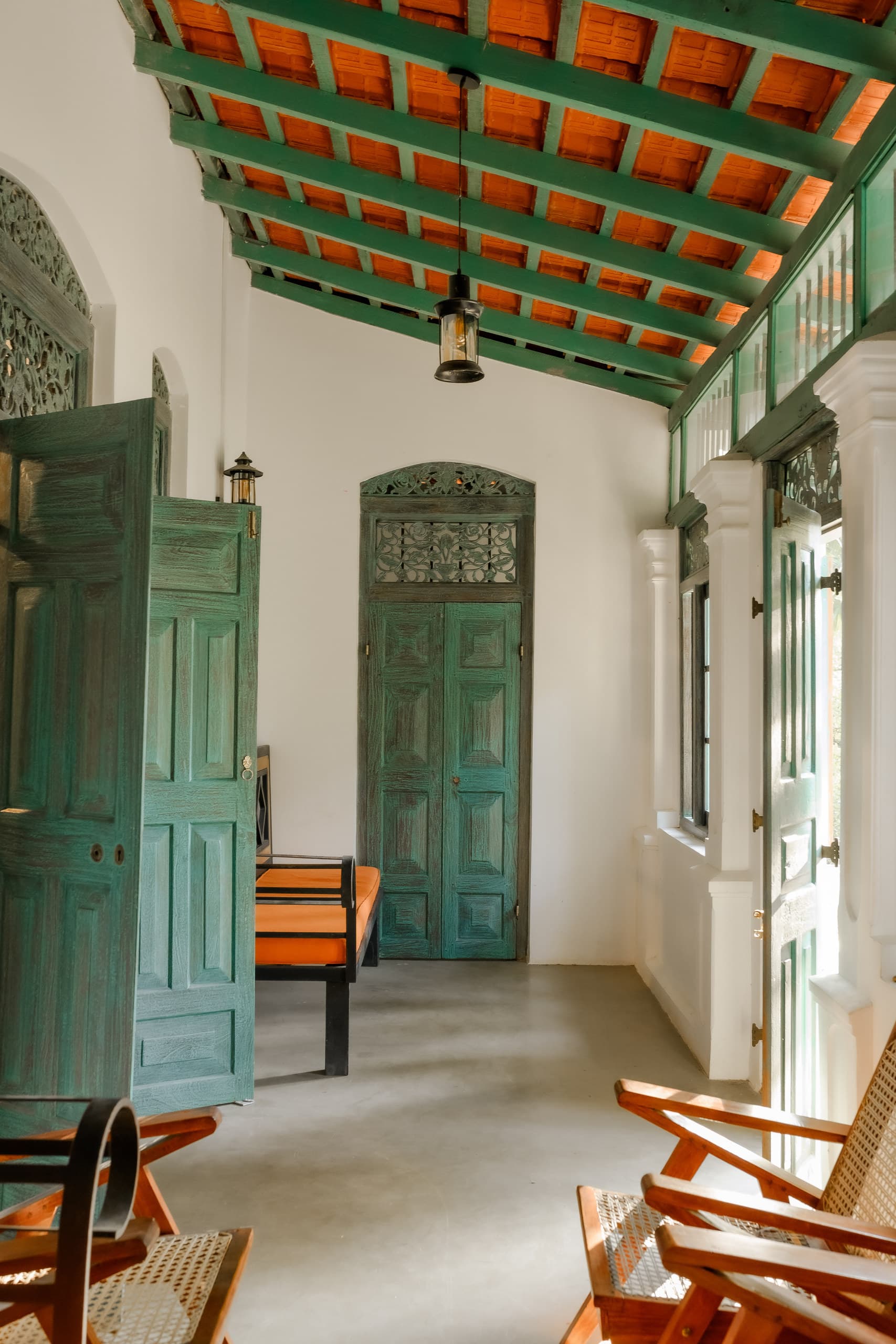 A corridor with a green timber ceiling, open green doors and cane chairs