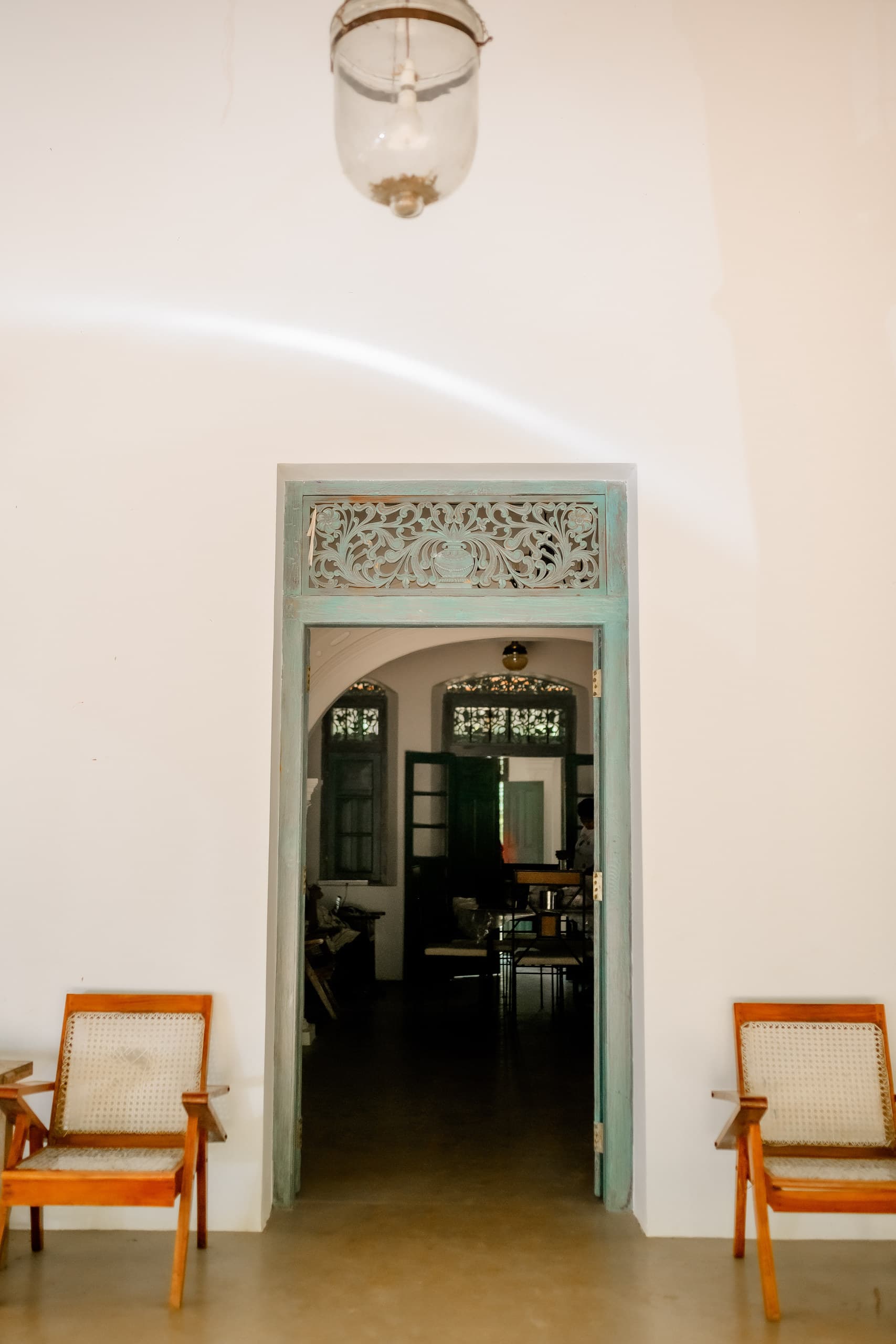 A carved timber fanlight above a green doorway, with two cane chairs