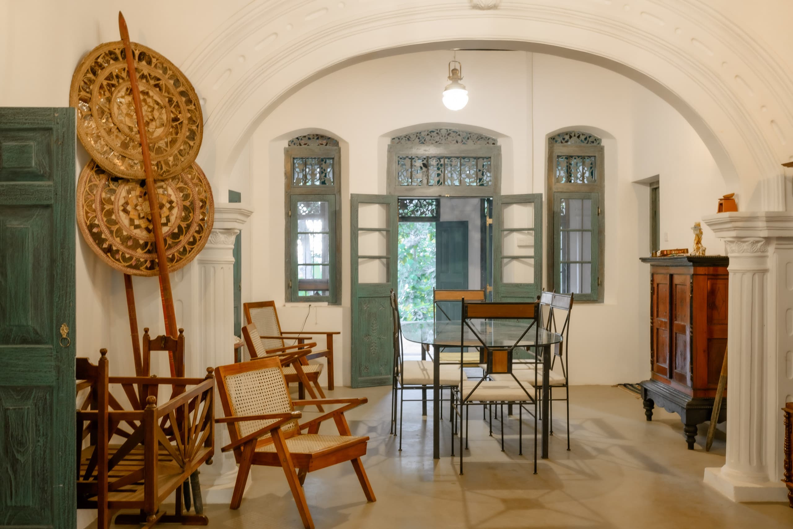 Large woven wall ornaments beside white columns and antique chairs