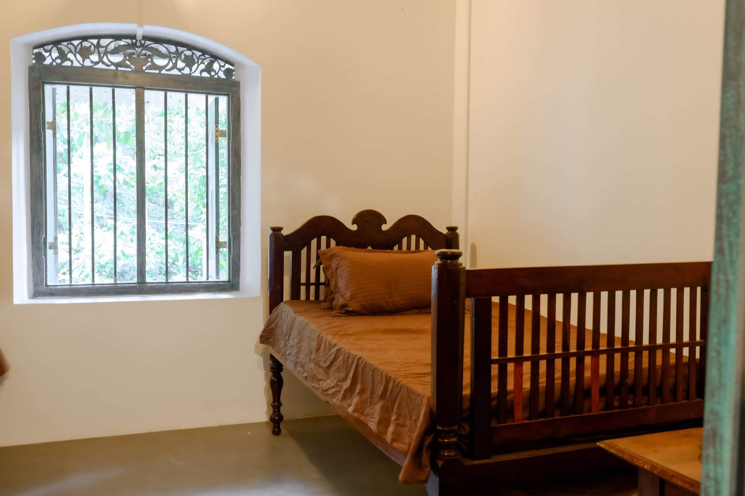 A carved timber bed beneath a barred arched window