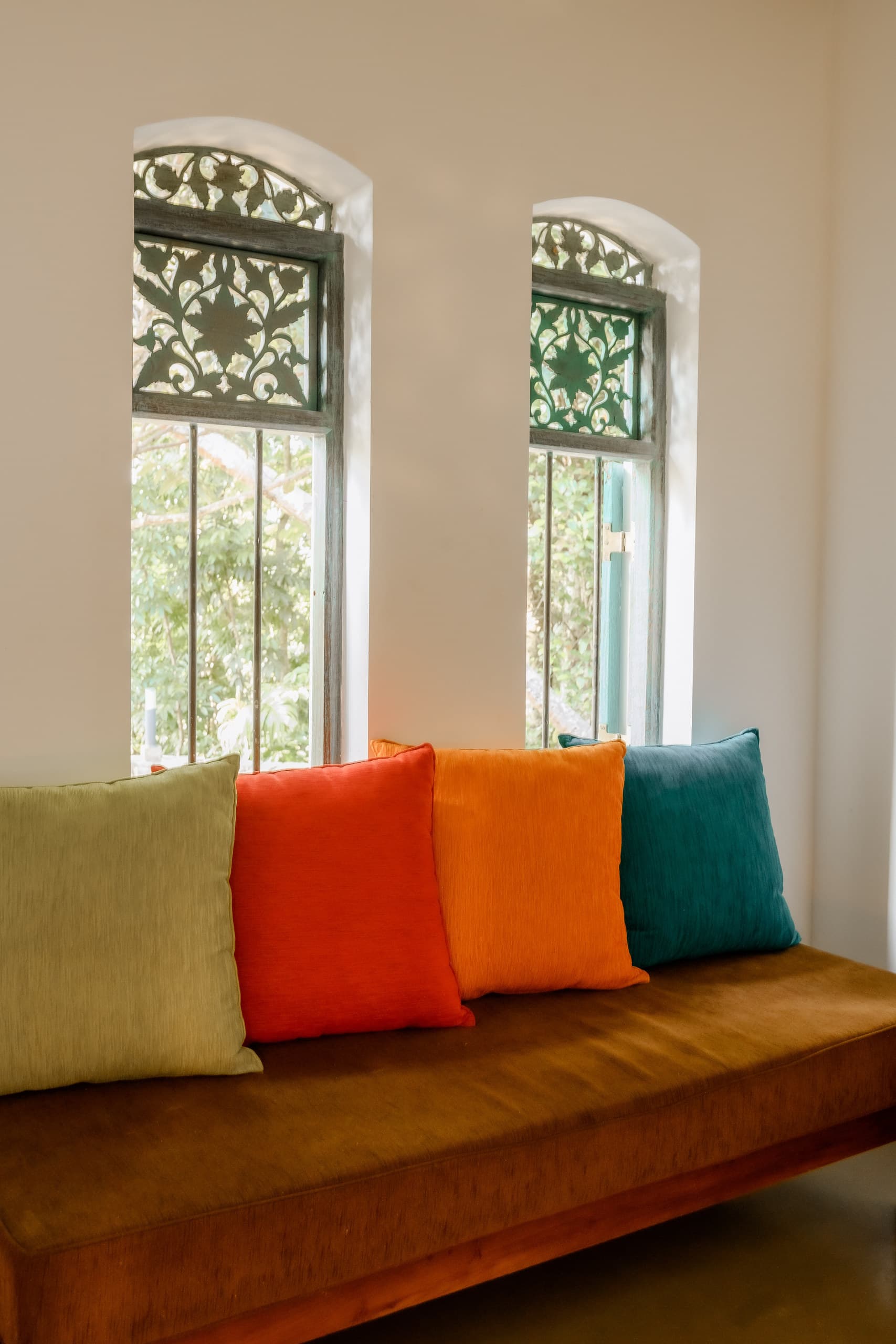 Two tall carved windows above a daybed with colourful cushions