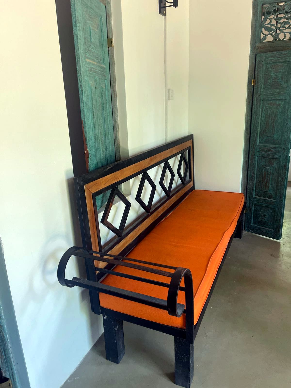 A bench with an orange cushion beside a carved green door