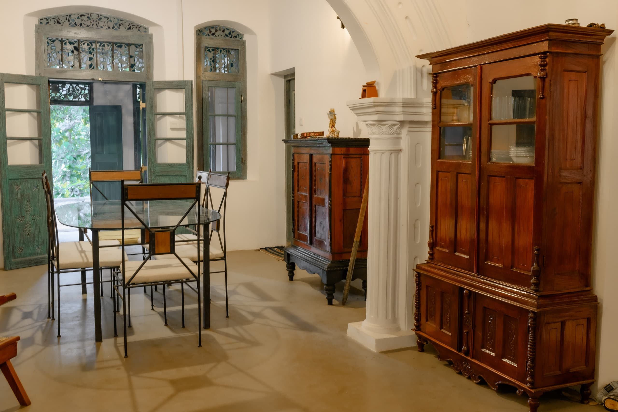 A glass table with cane chairs in the hall, beside a tall antique almirah