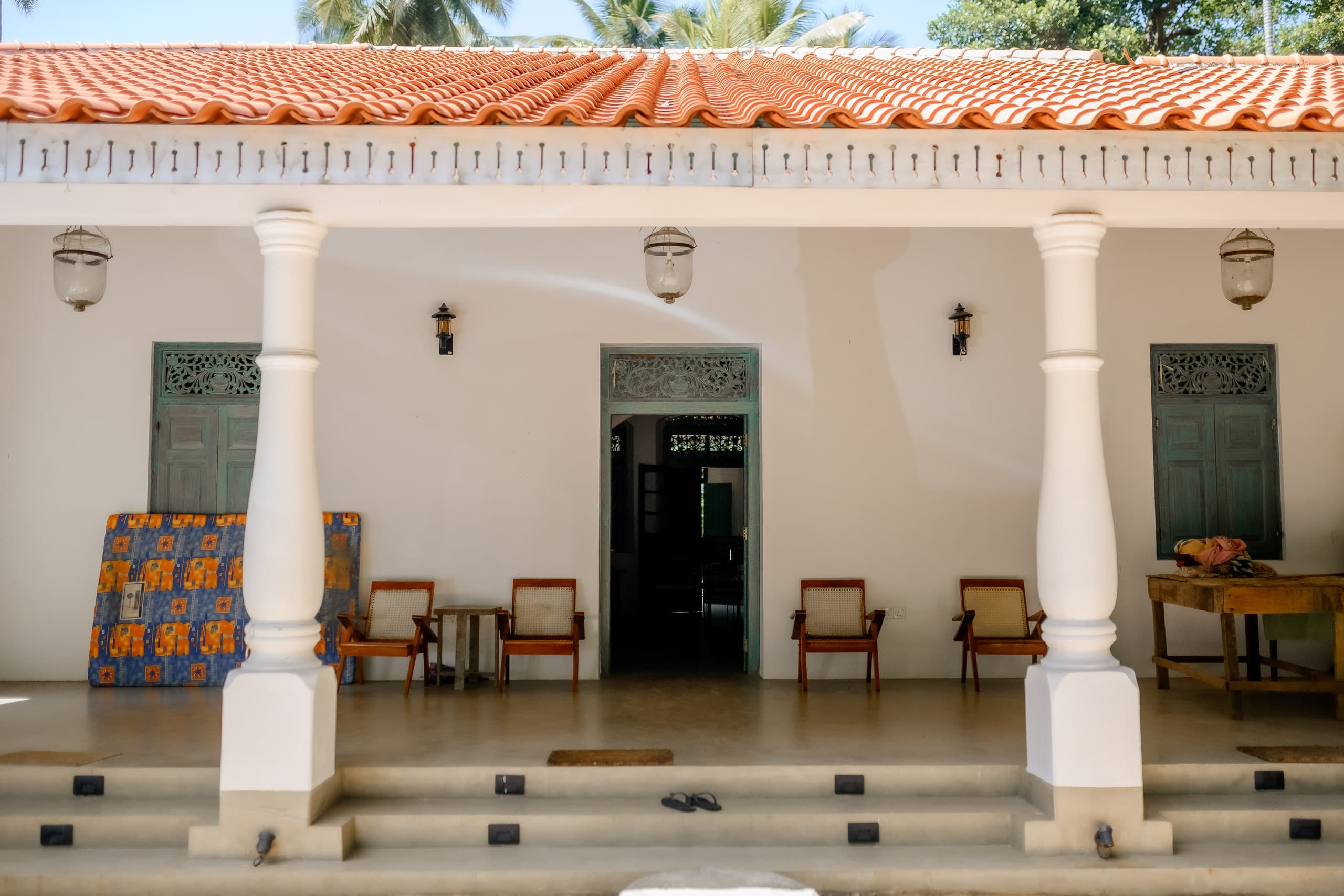 The front verandah of Dadakire Walawwa with white pillars, a tiled roof and a row of chairs